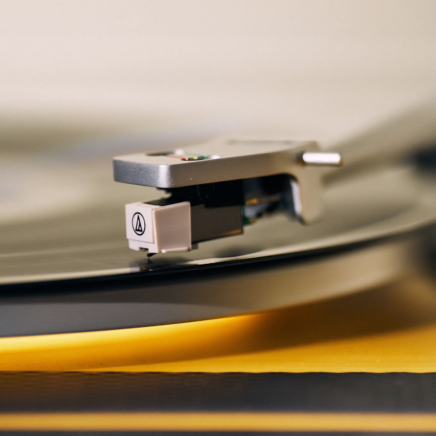 Gros plan sur l'aiguille d'une platine vinyle sur un disque vinyle. L'aiguille est argentée et beige. Le disque est noir avec un bord jaune.