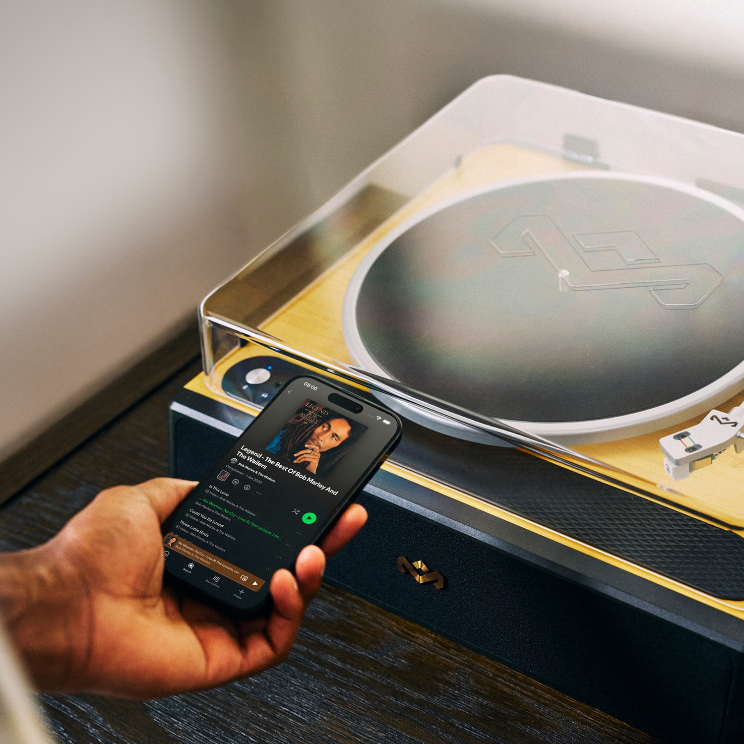 Une personne tient un téléphone montrant l'album de Bob Marley sur une platine. La platine est sur une surface en bois.