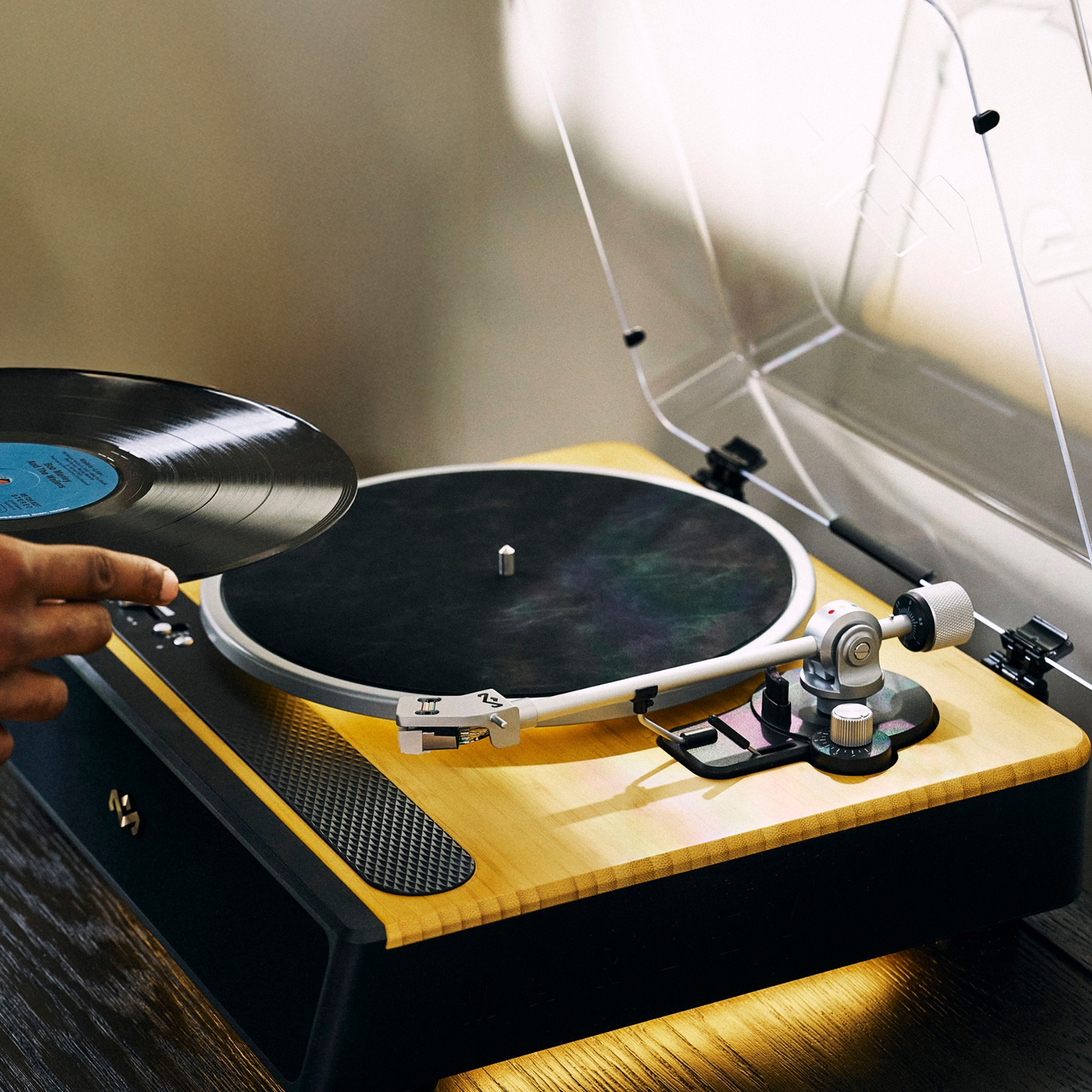 Une personne place un disque vinyle sur une platine vinyle en bois. La platine est noire et dorée avec un couvercle transparent.