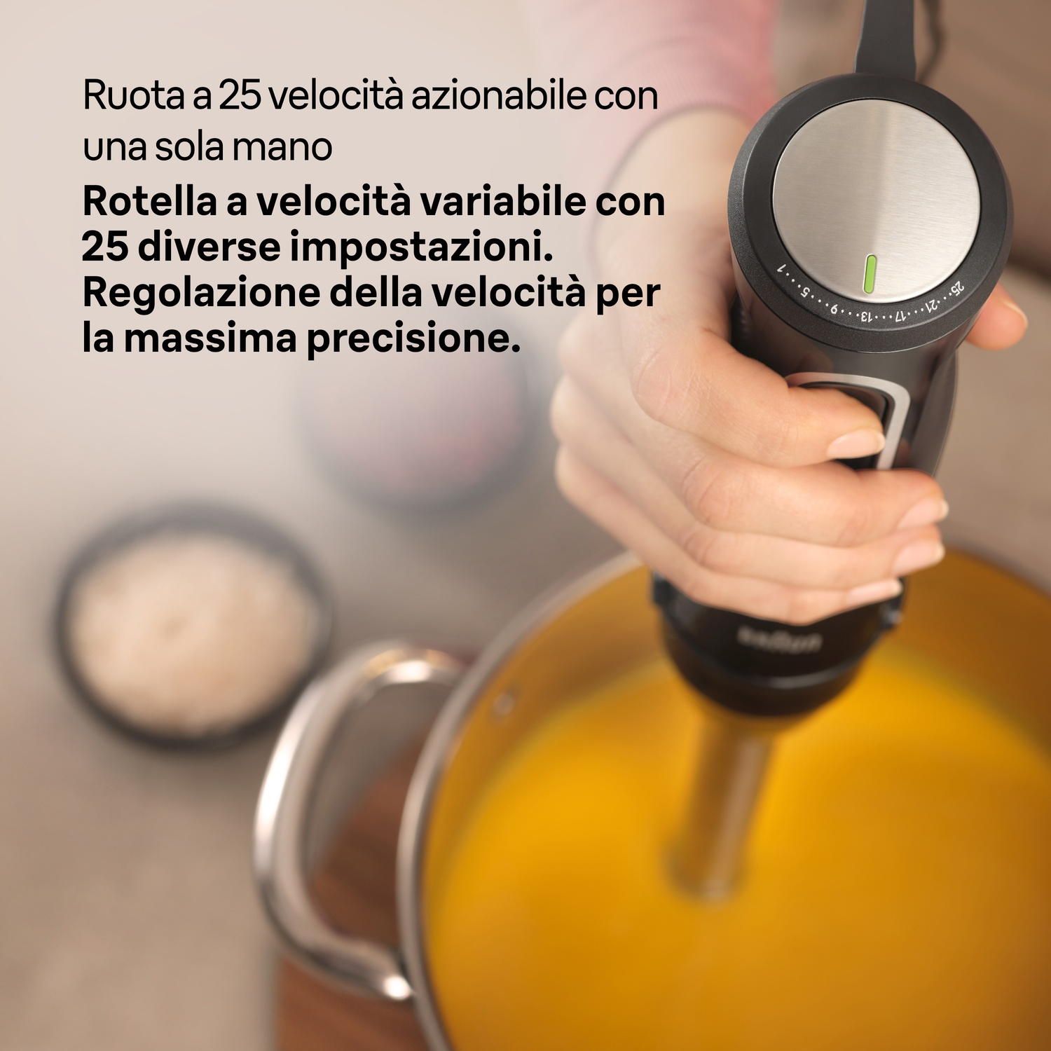 Una mano tiene un frullatore a immersione nero sopra una pentola di zuppa gialla. Il frullatore ha un quadrante.