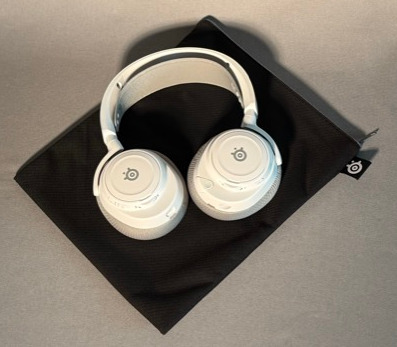 Białe słuchawki na czarnym etui, umieszczone na szarej powierzchni. Słuchawki są punktem centralnym, widoczne logo marki.