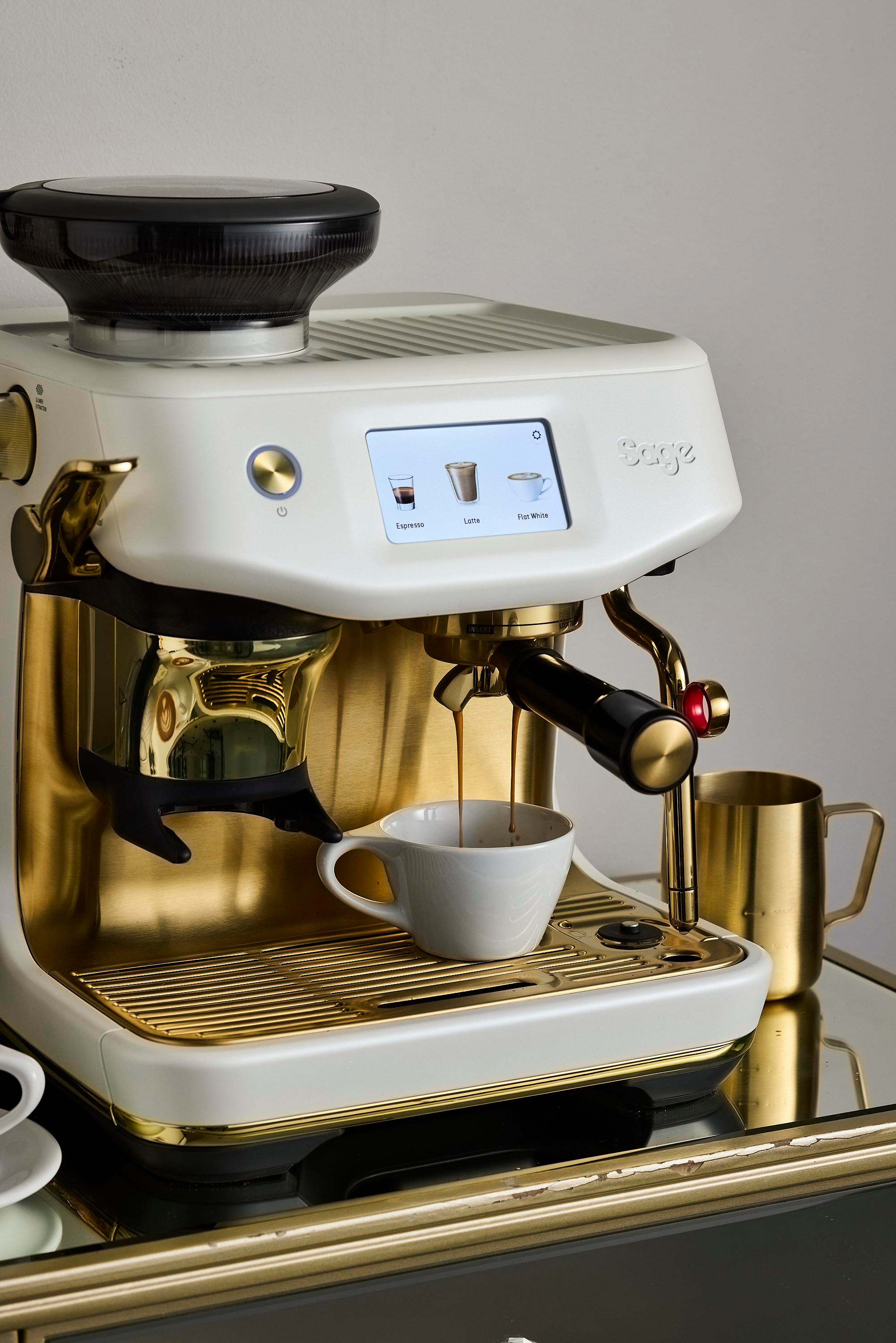 Espressomaschine mit Kaffee, der in eine weiße Tasse gegossen wird. Gold- und Weißschema. Flat White, Latte Optionen.