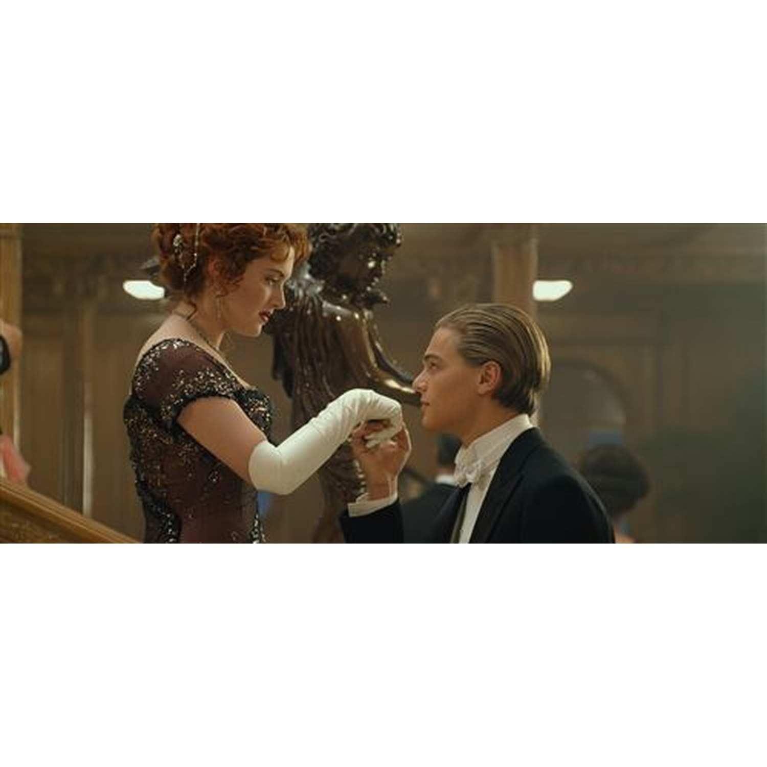 Een man in smoking houdt de hand van een vrouw vast, die een jurk en handschoenen draagt. Ze staan bij een trap en een standbeeld.