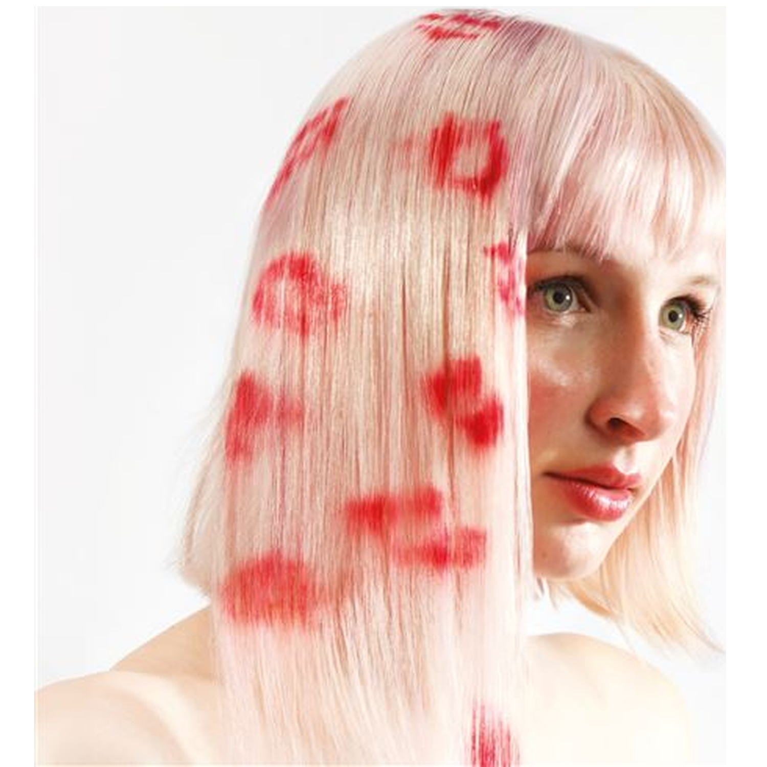 Femme aux cheveux blonds et empreintes de lèvres rouges. Elle regarde sur le côté. Fond blanc.