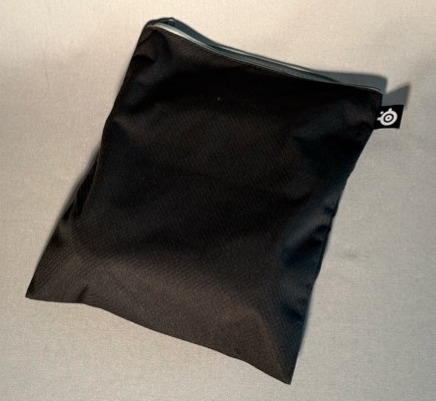 Czarna saszetka z zamkiem błyskawicznym na szarej powierzchni. Widoczne małe białe logo.