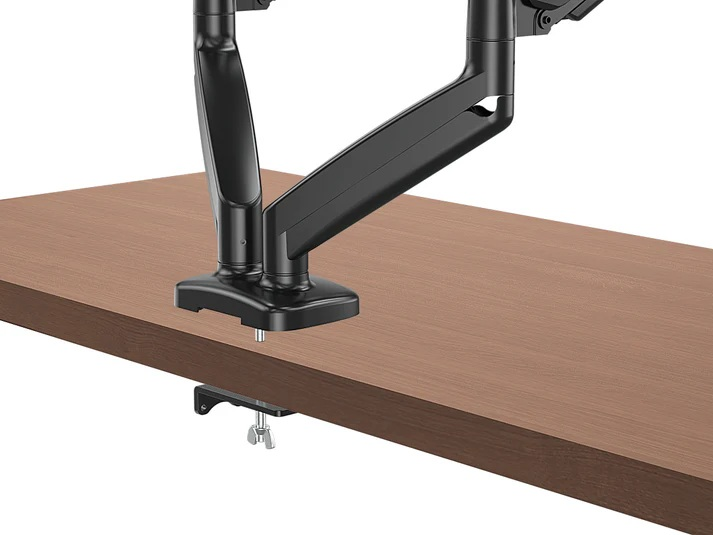 Czarny uchwyt do monitora zamontowany na drewnianym biurku. Zacisk mocuje ramię do biurka. Tło jest białe.