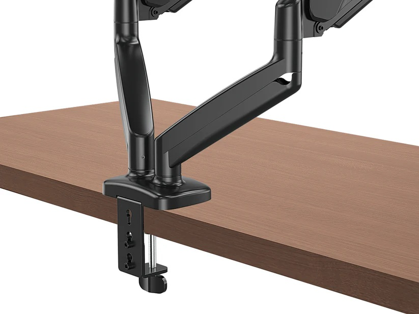 Czarny podwójny uchwyt do monitora jest przymocowany do drewnianego biurka. Ramię ma kilka przegubów i zacisk.