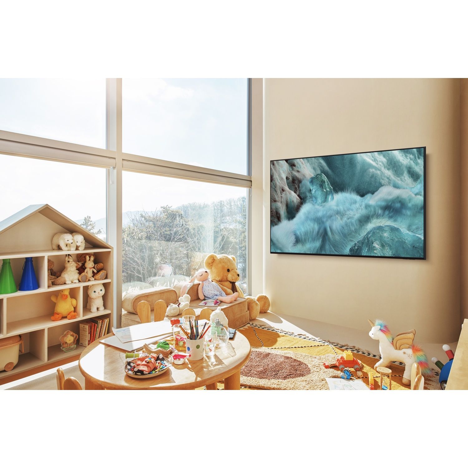 A playroom with a large window, TV, and toys. A wooden table with art supplies. A large teddy bear and unicorn are visible.