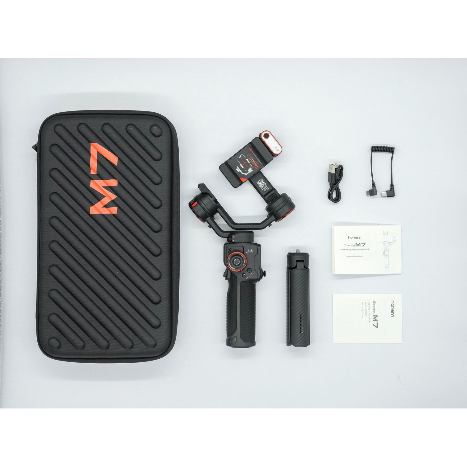 Un kit gimbal Hohem Steady M7 nero con accessori. Include custodia, manuali, cavi e una piccola maniglia a treppiede su una superficie bianca.