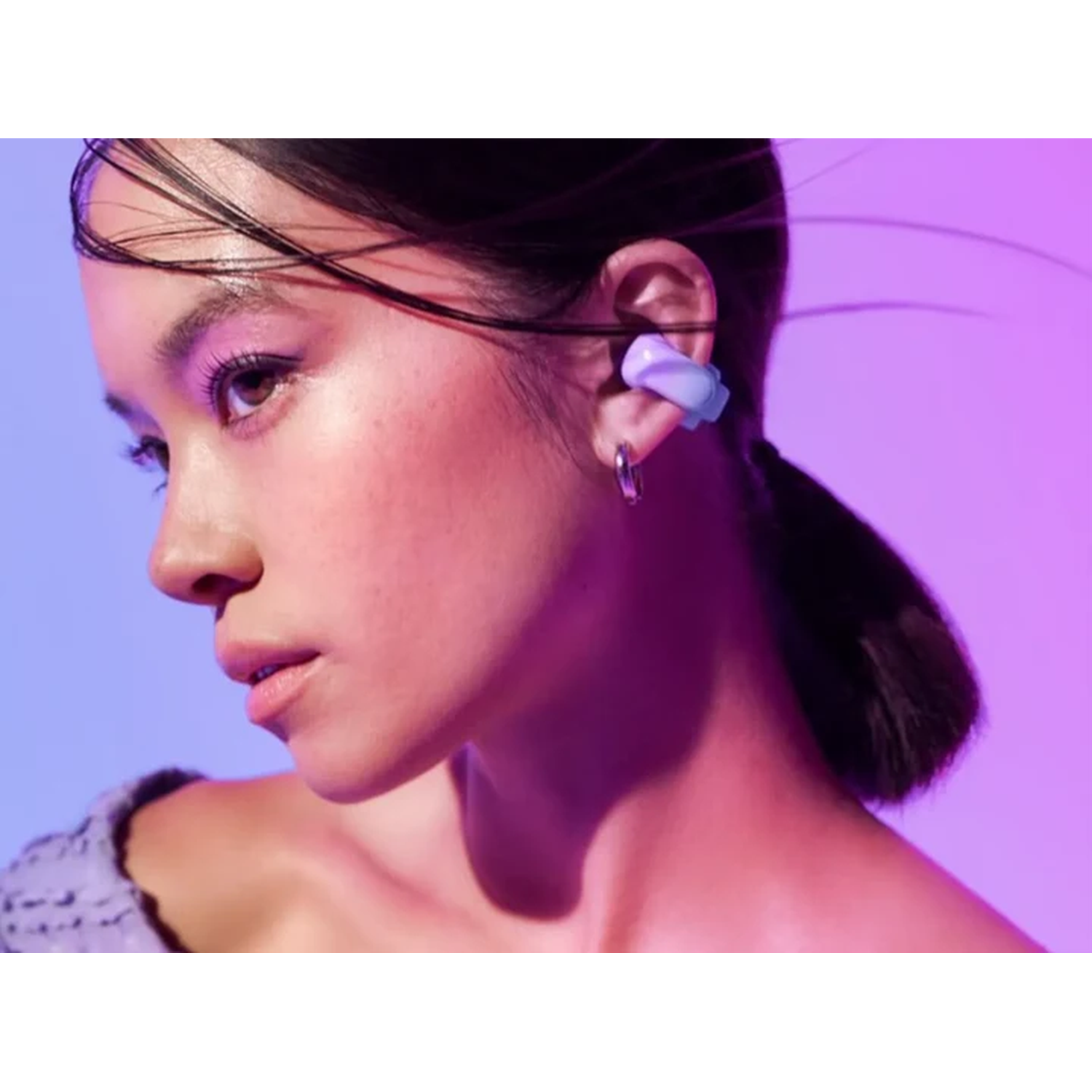 A woman with makeup wears an earring and earbud, with dark hair, looking left. Purple and blue gradient background.