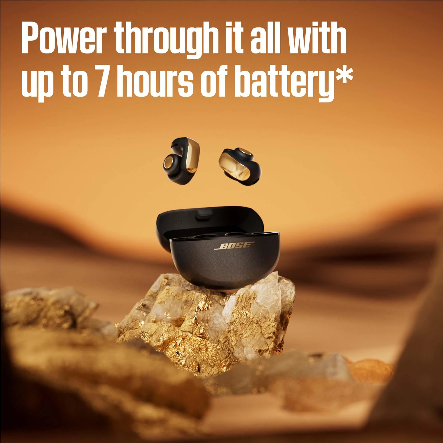 Oordopjes, oplaadcase op steen, gouden accenten. Tekst: Power through it all with up to 7 hours of battery. Bose-logo.
