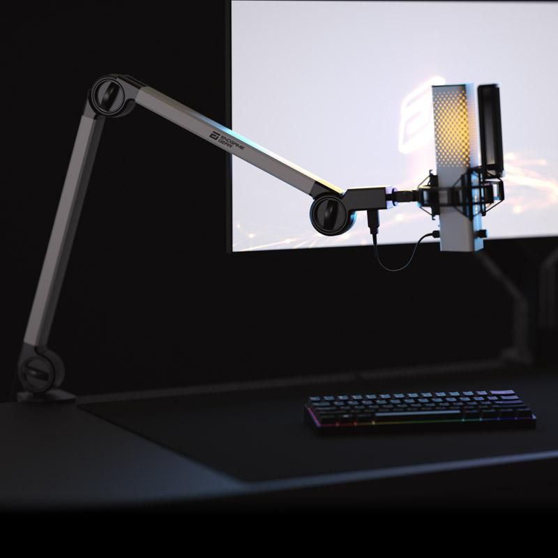 Ein Mikrofon ist an einem Arm vor einem Monitor montiert. Eine Tastatur liegt auf dem Tisch unter dem Monitor. Die Szene ist dunkel.