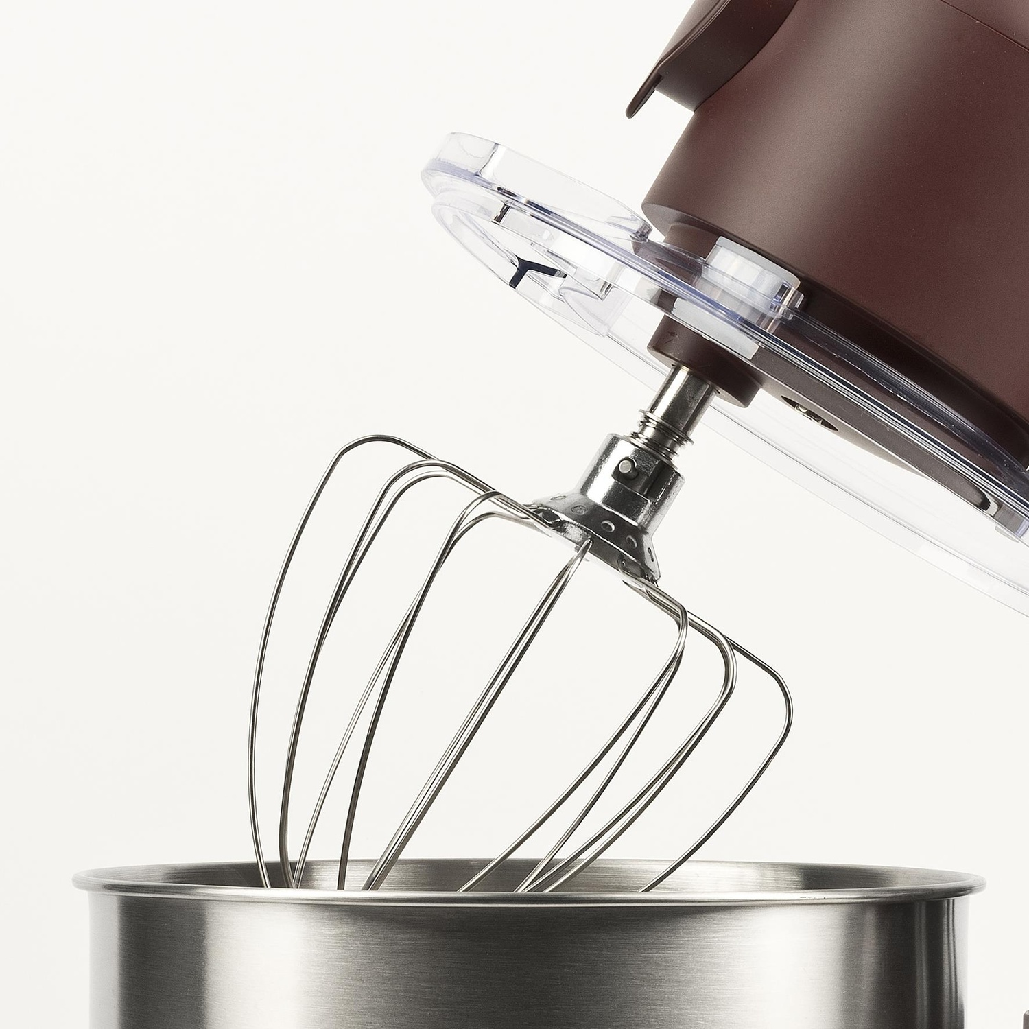 Primo piano di un mixer da cucina marrone con frusta. La frusta è sopra una ciotola in acciaio inossidabile, coperchio in plastica trasparente.