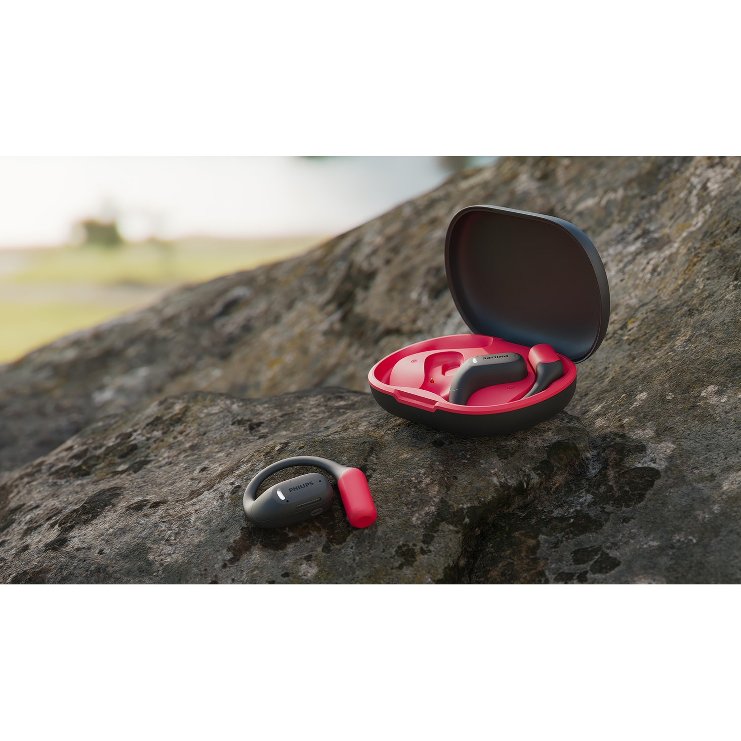 Auricolari e custodia su una roccia. Custodia aperta, auricolari rossi all'interno. Un auricolare accanto. Sfondo verde sfocato.