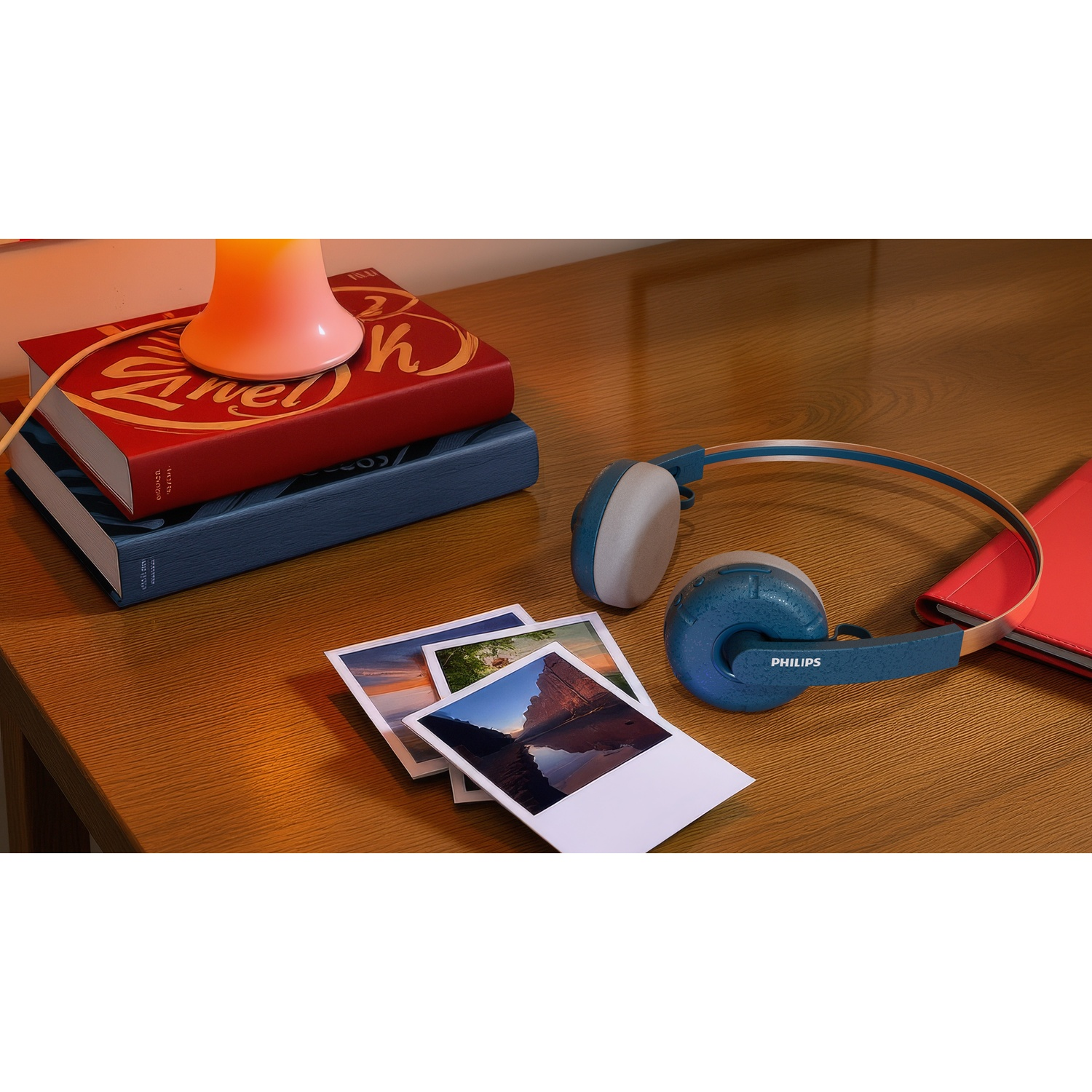 Cuffie, libri, foto e una lampada su una scrivania di legno. Le cuffie sono blu e grigie. I libri sono rossi e blu. Le foto mostrano paesaggi.