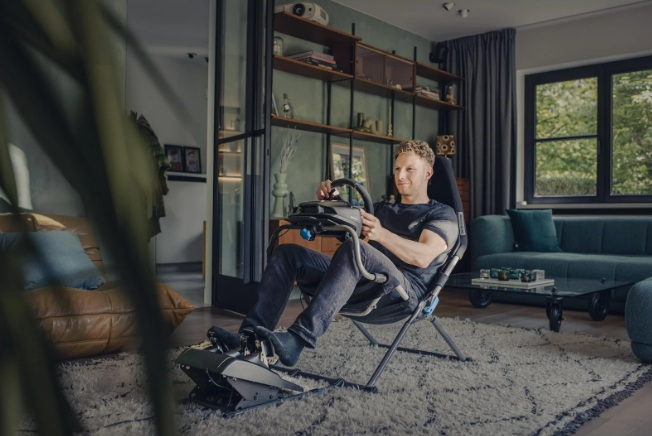 Mężczyzna siedzi w fotelu wyścigowym z kierownicą i pedałami, gra w grę wideo.