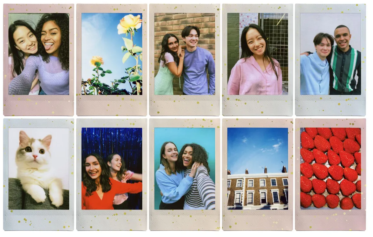 Due donne sorridenti, una che tira fuori la lingua, in una polaroid. Lo sfondo è di un colore morbido e caldo.