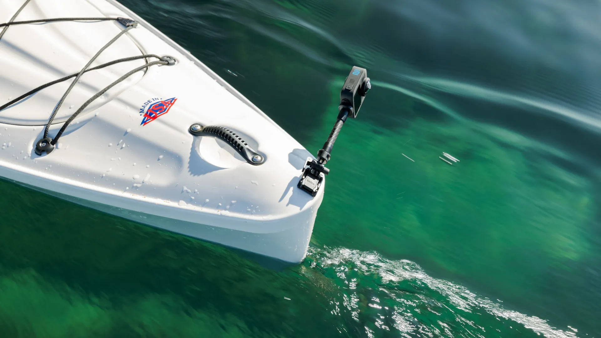 L'avant d'un kayak blanc flotte sur l'eau verte. Une caméra sur un bras noir s'étend. Le kayak a des cordes et une poignée. Logo Made in USA.