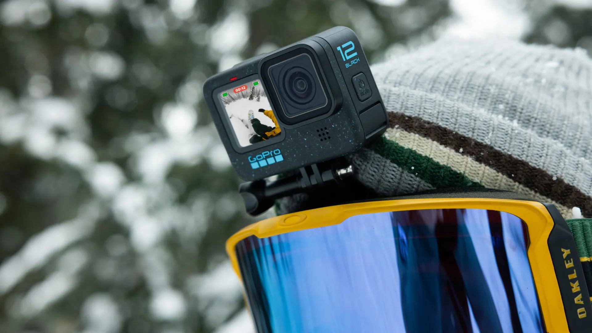 Fotocamera GoPro attaccata a un casco da sci, che mostra uno sciatore su una pista innevata. Occhiali gialli e berretto grigio visibili.