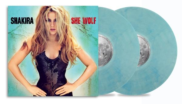 Shakira-Albumcover und zwei hellblaue Schallplatten. Shakira in schwarzem Kleid, Albumtitel "She Wolf".