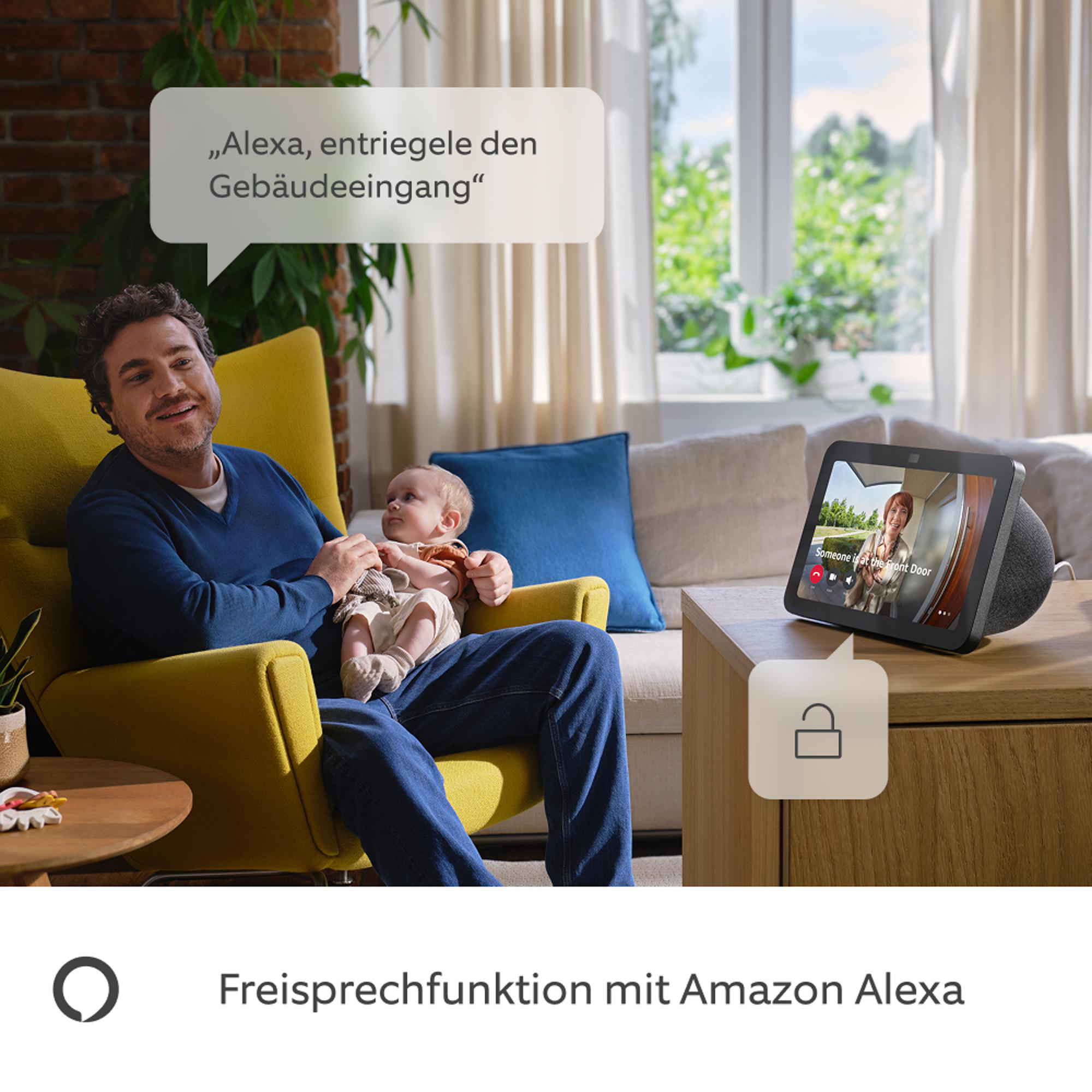 Mann mit Baby, der Alexa zum Entriegeln der Tür benutzt. Smart Display zeigt jemanden an der Haustür. Gelber Stuhl.
