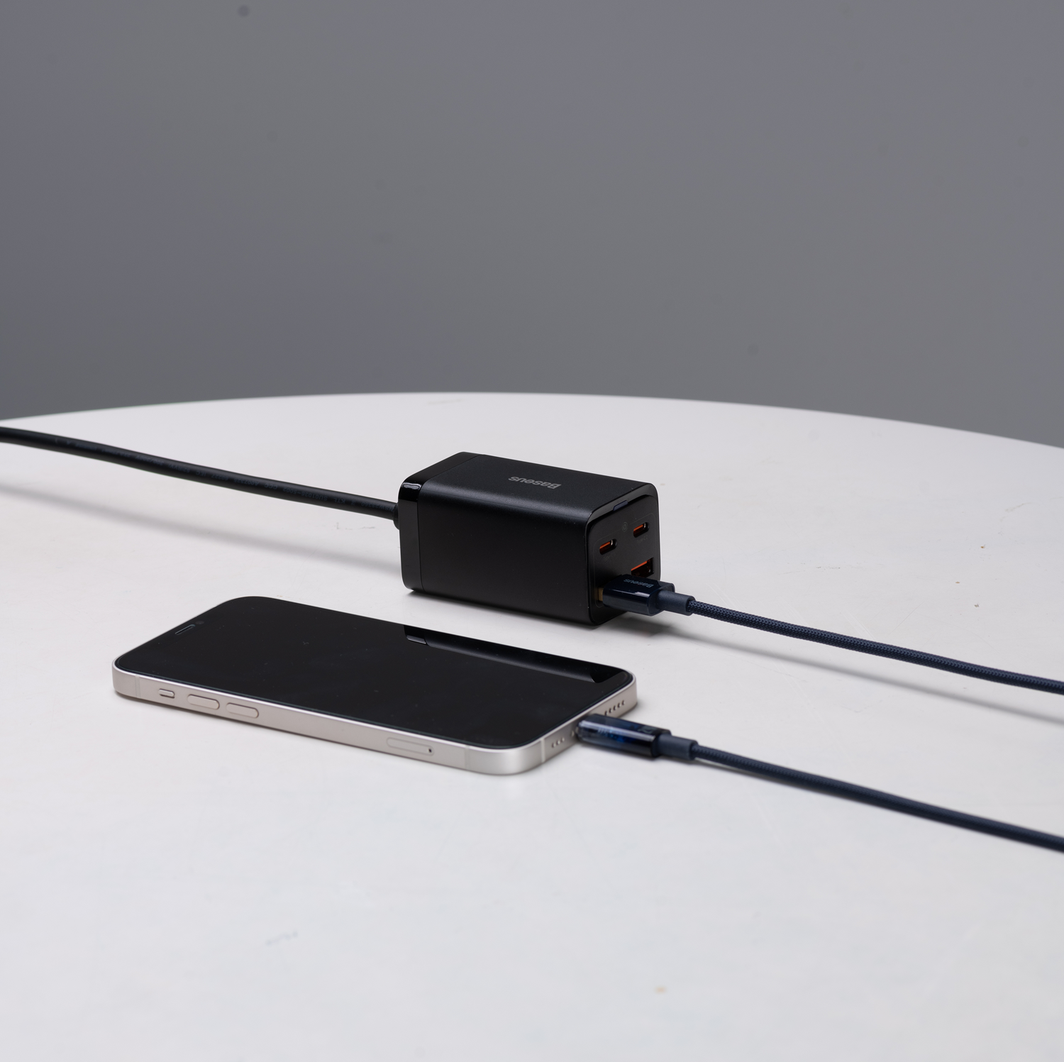 Un teléfono negro está conectado a un cargador negro mediante un cable azul. El cargador está sobre una superficie blanca.
