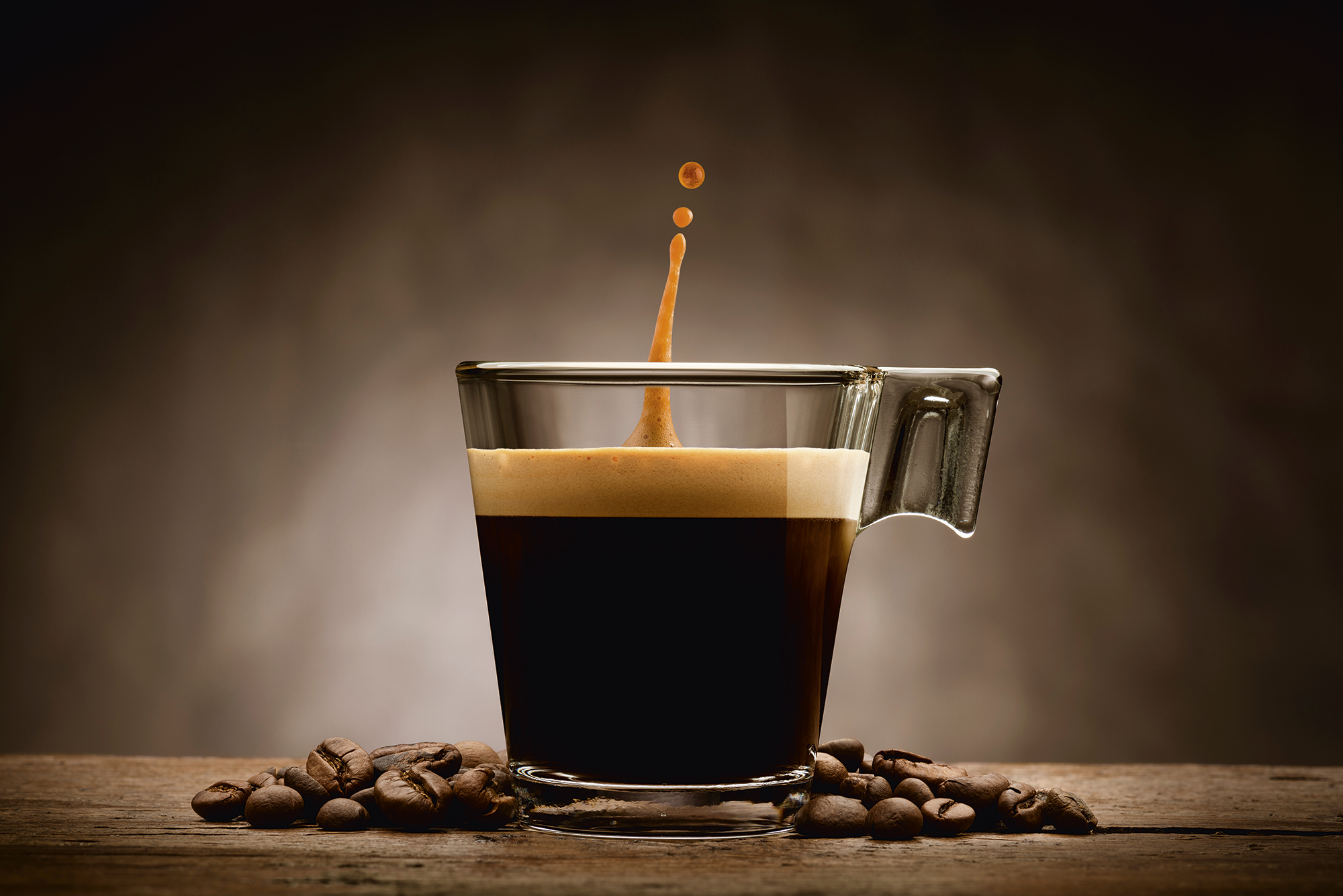 Espresso in einem Glas, Kaffeebohnen auf einem Holztisch, Kaffeespritzer in der Luft.