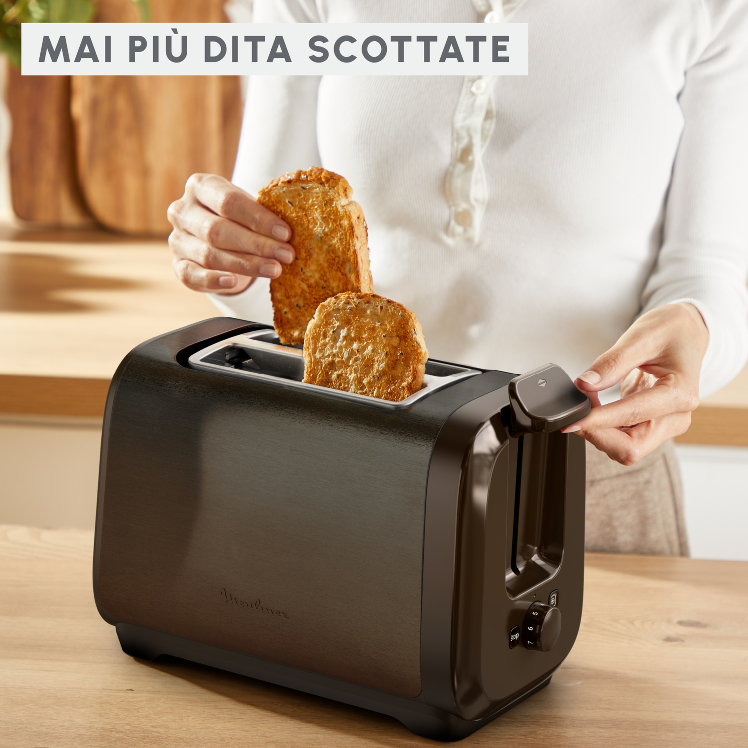 Una persona toglie pane tostato da un tostapane nero. Il tostapane è su un tavolo di legno. Il testo dice 'MAI PIÙ DITA SCOTTATE'.