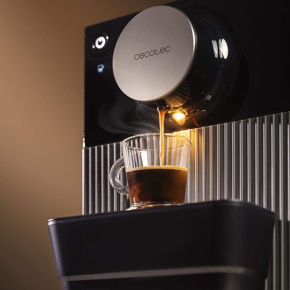 Cafetera dispensando café en una taza de vidrio. La máquina es negra y plateada. El café es marrón oscuro.