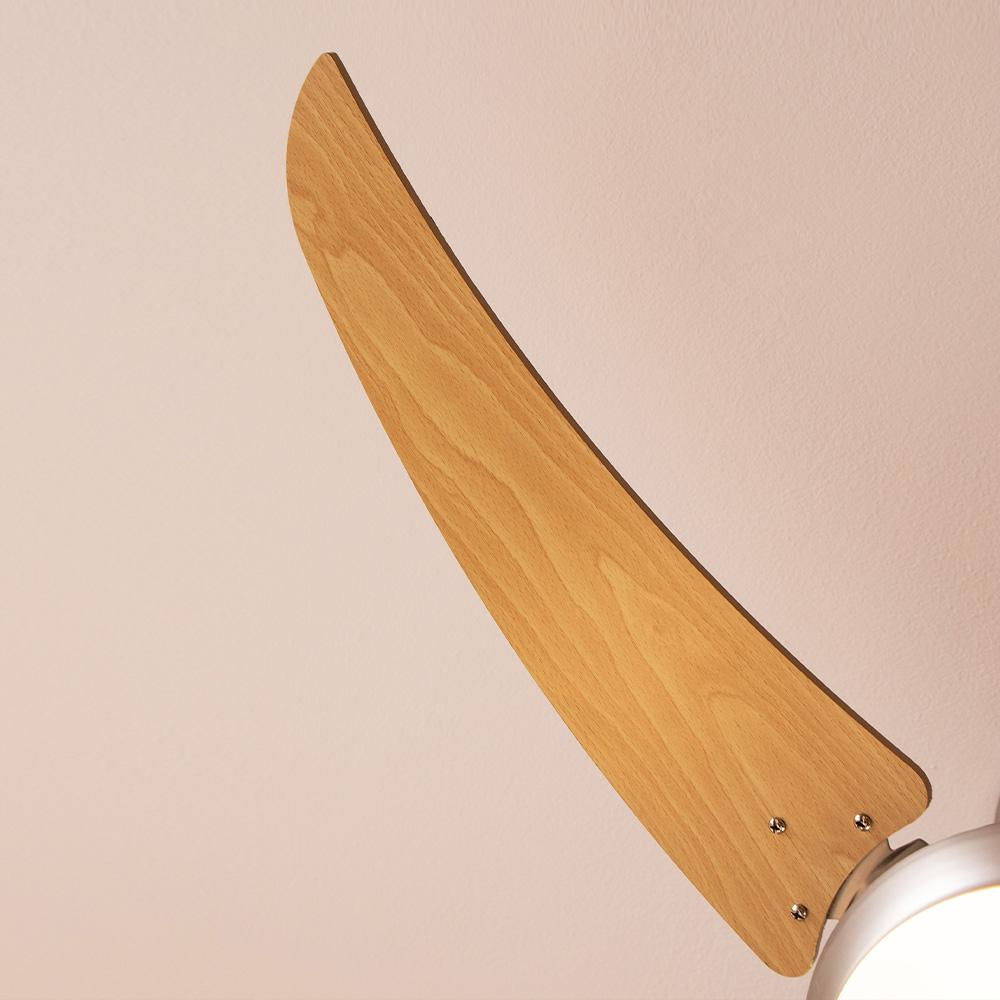 Una aspa de ventilador de techo de madera está en ángulo sobre un techo rosa pálido. La hoja tiene veta de madera clara. El motor del ventilador es visible.
