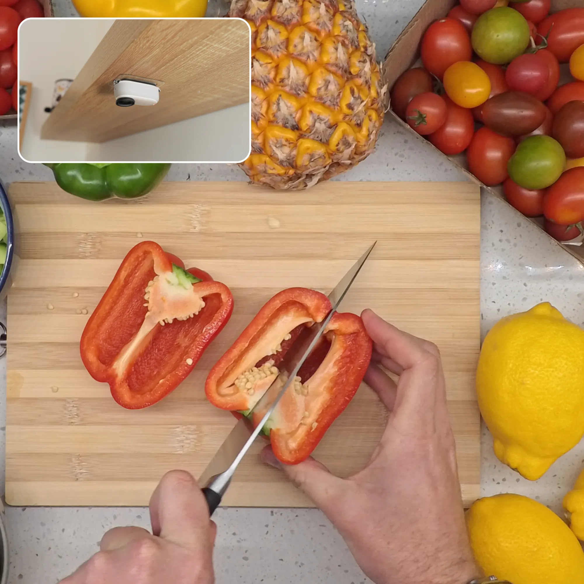 Eine Person schneidet eine rote Paprika auf einem Holzbrett. Im Hintergrund sind andere Gemüse und eine Ananas.