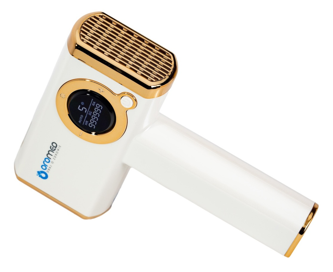 Biało-złote urządzenie medyczne, prawdopodobnie laser. Ma wyświetlacz pokazujący liczby i tekst. Urządzenie znajduje się na białym tle.