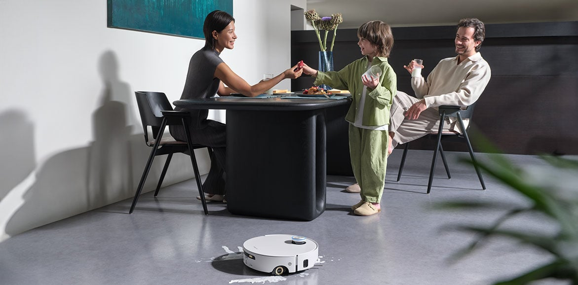 Rodzina przy stole, dziecko częstuje jedzeniem. Robot sprząta podłogę. Nowoczesna jadalnia ze sztuką.