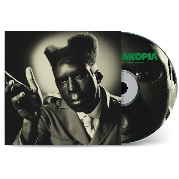 Albumcover mit einer maskierten Person und einer CD mit 'AKOPIA'. Die Person im Anzug zeigt.