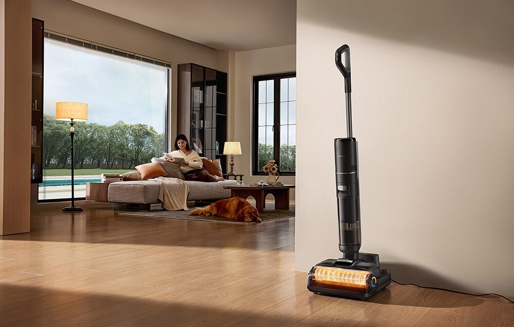 Kobieta czyta na sofie, pies leży na podłodze. Odkurzacz stoi obok. Lampa i okno są w tle.