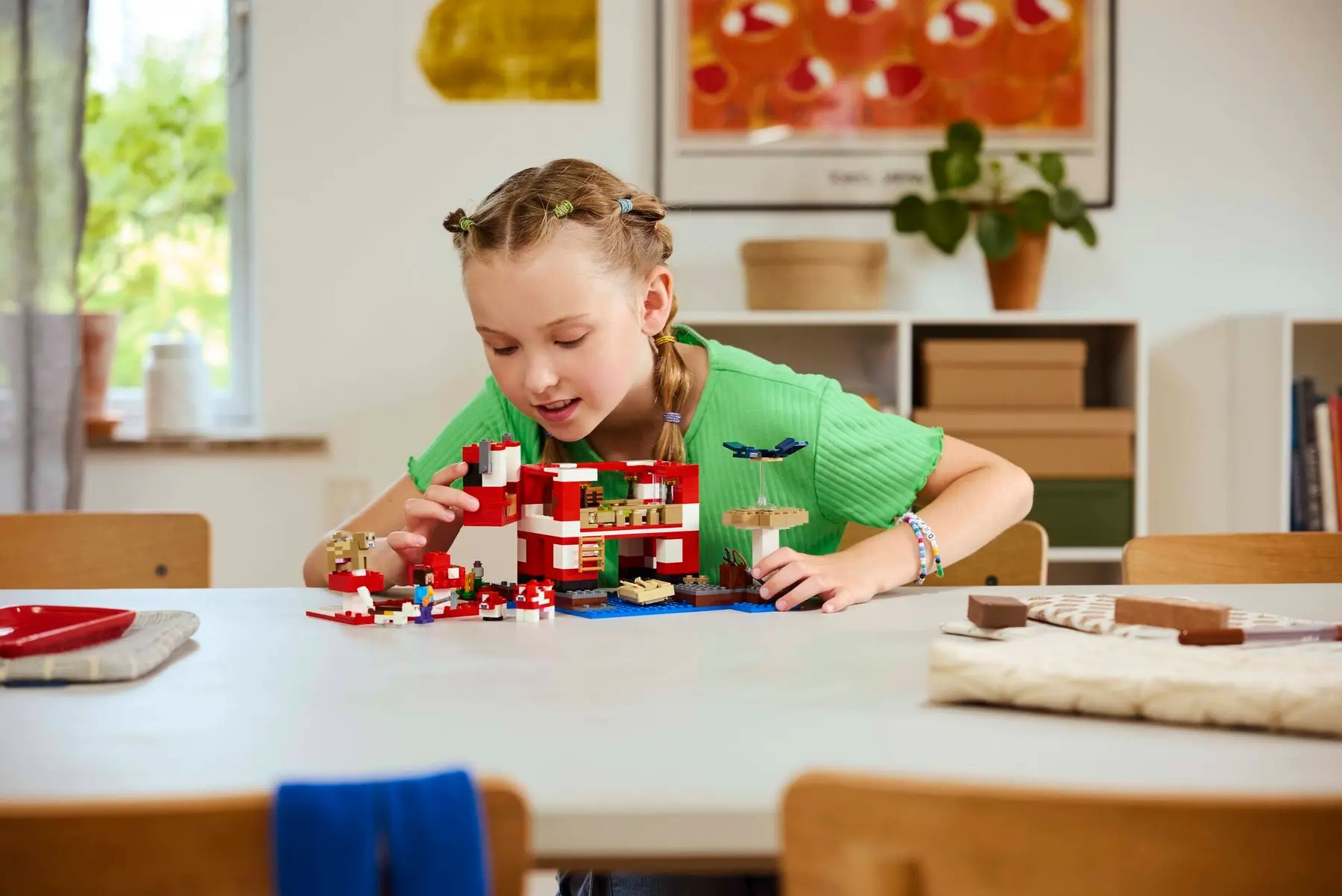 Dziewczyna buduje z Lego na stole. Czerwona i biała konstrukcja Lego. Samolot jest zawieszony. Obecne są również inne elementy Lego.