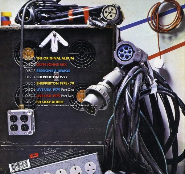 Nahaufnahme eines Tontechnikpanels mit Kabeln und Steckern. Text listet Albumtracks auf. Kabel im Vordergrund, weiße und blaue Streifen im Hintergrund.