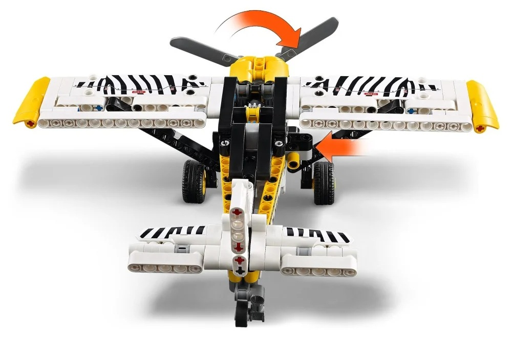 Zabawkowy samolot wykonany z białych, żółtych i czarnych klocków. Ma śmigło i koła, strzałki wskazujące ruch.