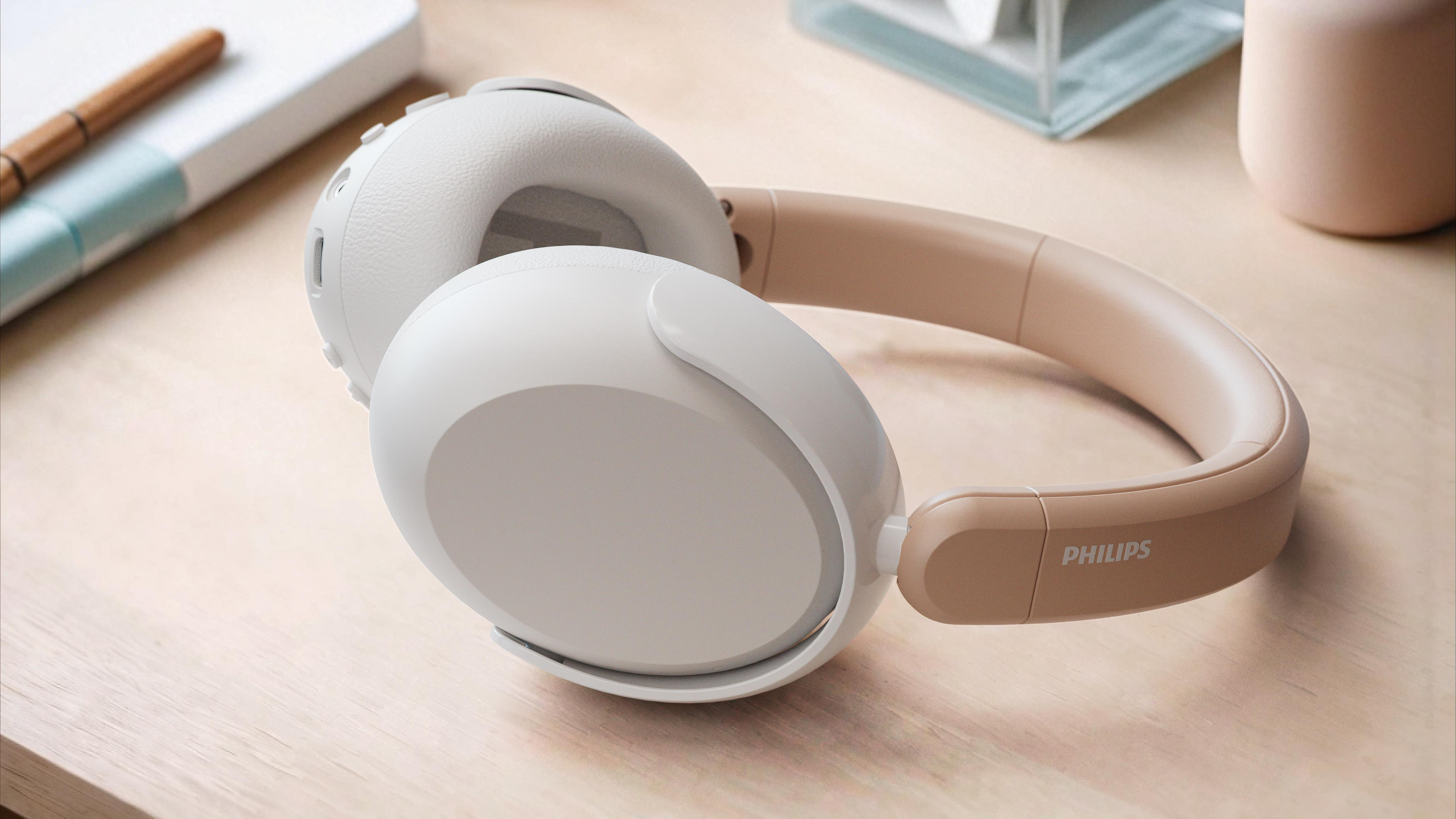 Over-Ear-Kopfhörer auf Holzoberfläche. Die Kopfhörer sind beige und weiß. Ein Notizbuch und Stift sind im Hintergrund.