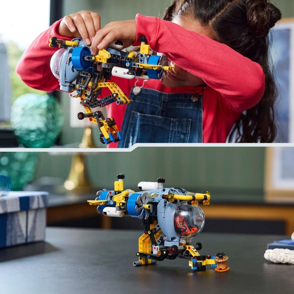 Dziecko składa niebiesko-żółtą zabawkę-łódź podwodną. Zabawka stoi na biurku. Dziecko ma na sobie czerwoną koszulę i dżinsowe ogrodniczki.