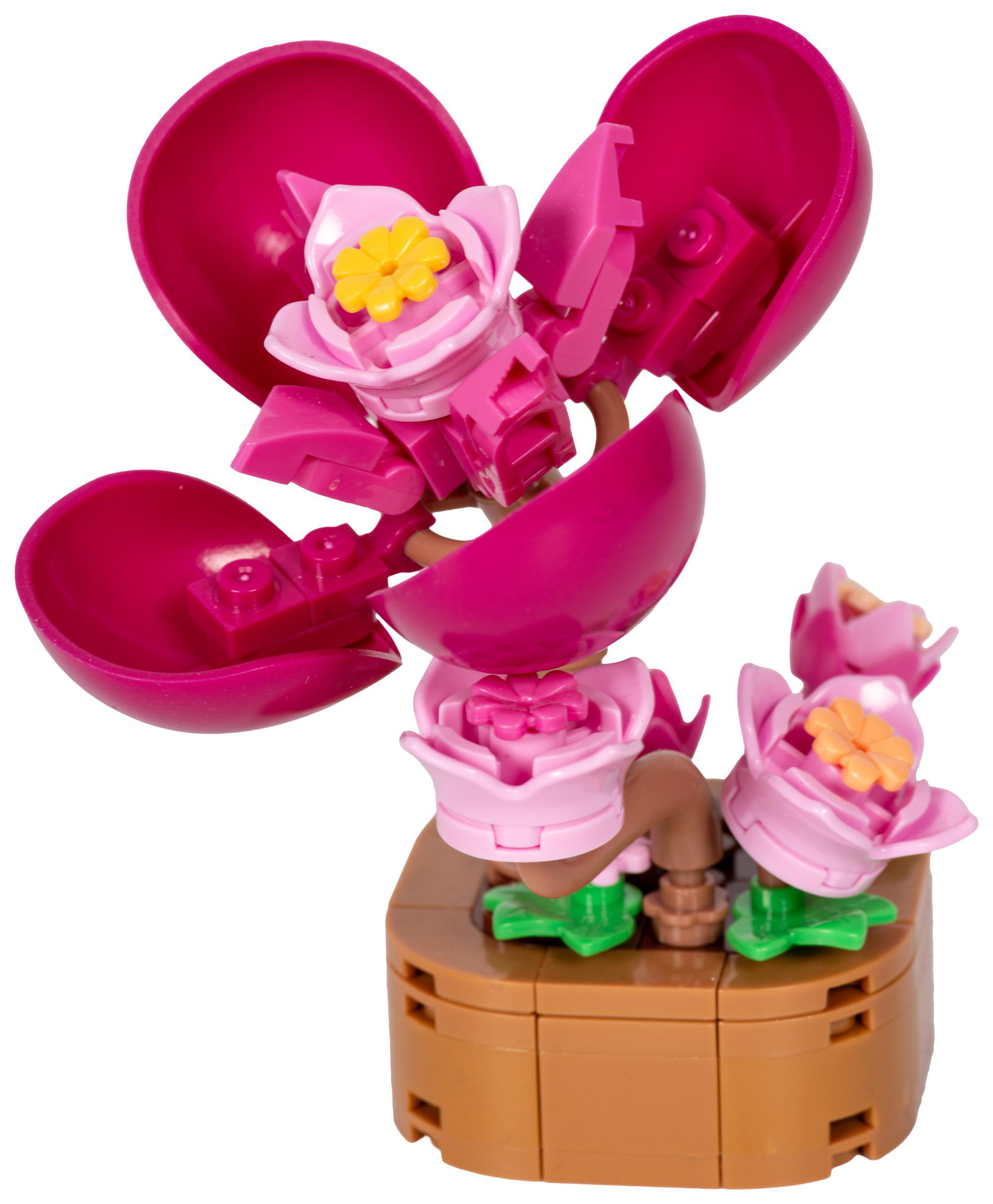 Ein Lego-Blumenspielzeug mit rosa Blütenblättern und einem gelben Zentrum auf brauner Basis und weißem Hintergrund.