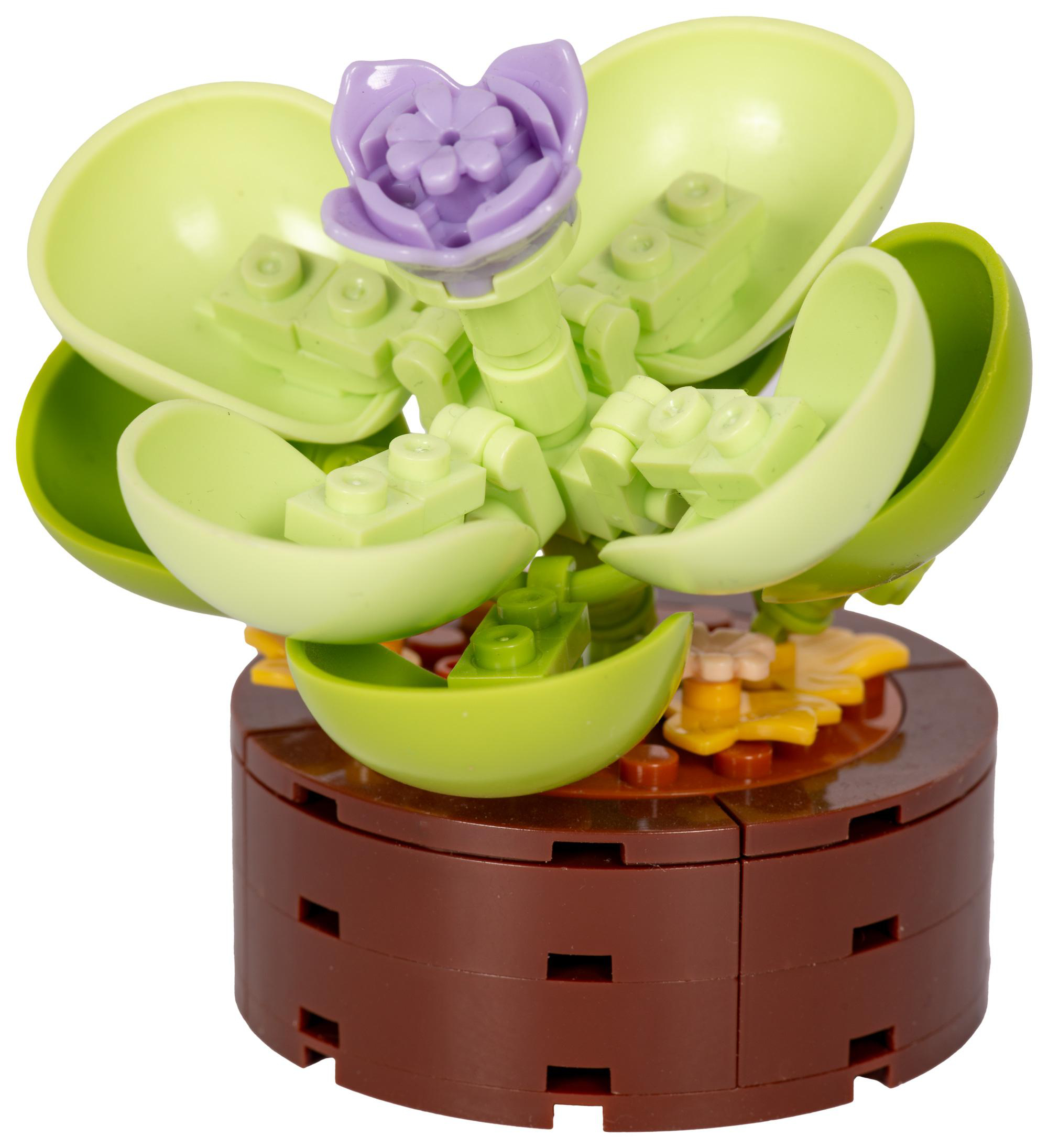 Eine Lego-Blume mit grünen Blättern und einer lila Blume, die auf einem braunen Topf steht. Weißer Hintergrund.