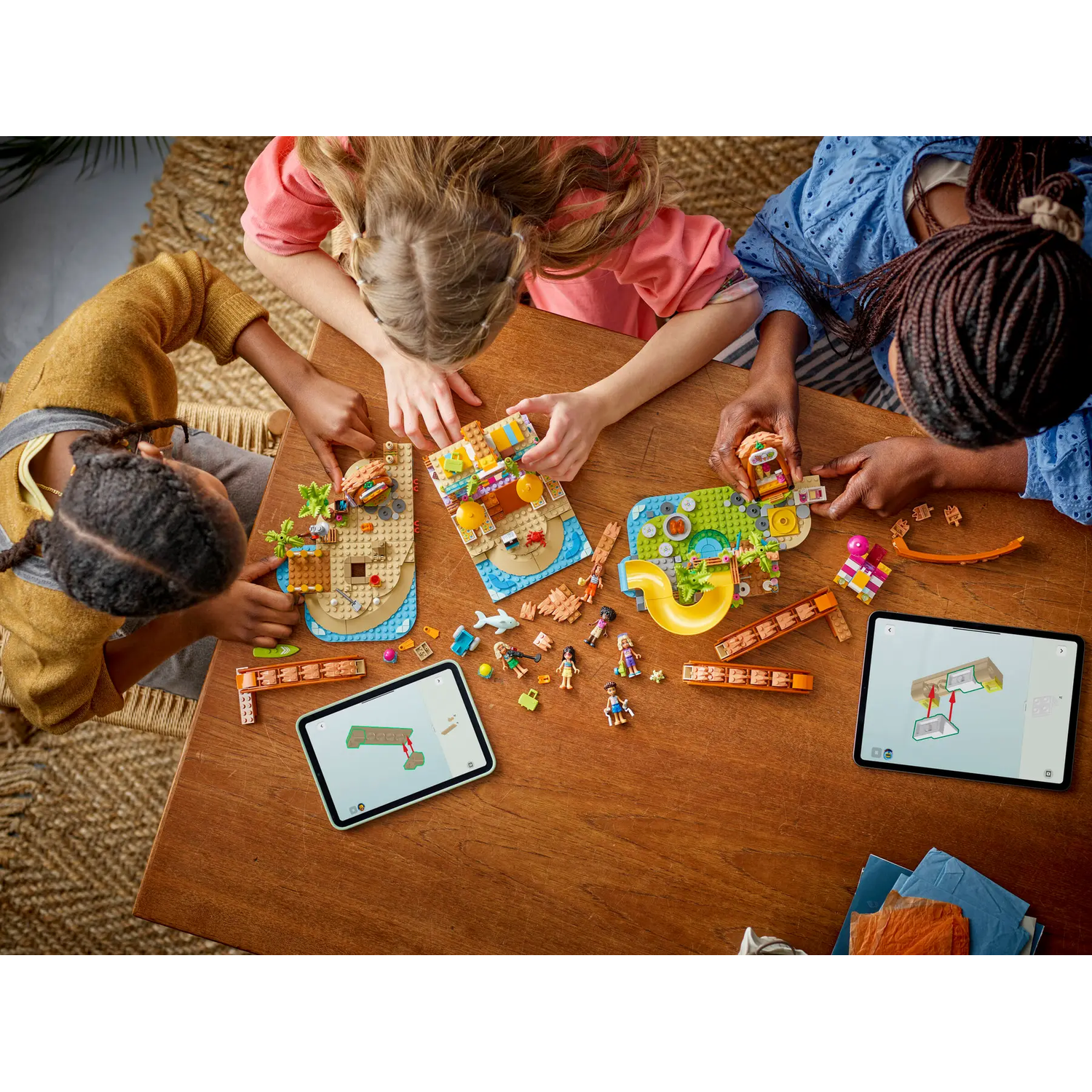 Three children building Lego sets on a wooden table. Sets include beach scenes and a water slide. Tablets show instructions.