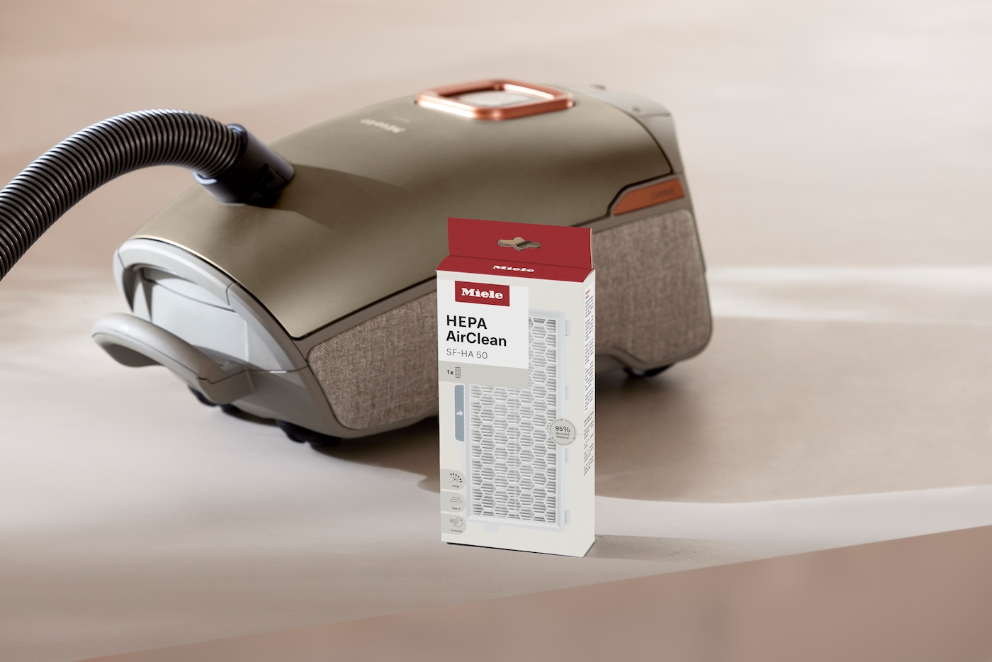 Ein beiger Miele-Staubsauger und eine Filterbox. Auf der Box steht 'HEPA AirClean SF-HA 50'. Der Staubsauger ist teilweise sichtbar.