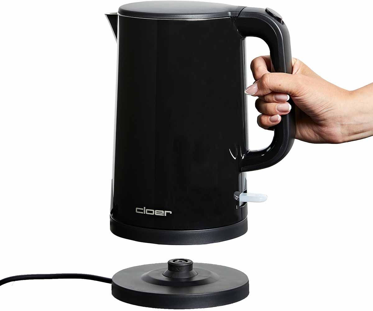 Ein schwarzer Wasserkocher wird von einer Hand gehalten. Er steht auf einem schwarzen Sockel. Der Markenname 'cloer' ist sichtbar.