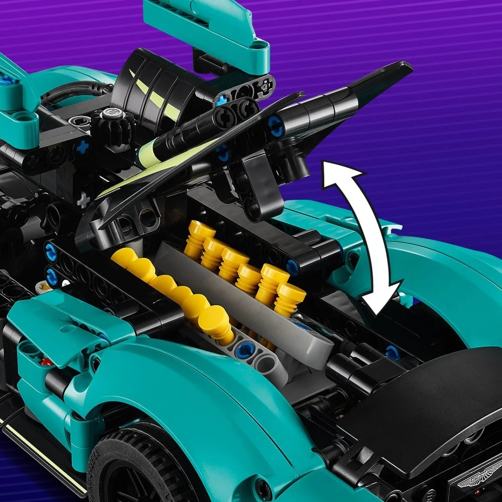 Niebiesko-czarny samochód Lego z otwartą komorą silnika. Widoczne są żółte detale. Strzałka wskazuje otwarcie maski.