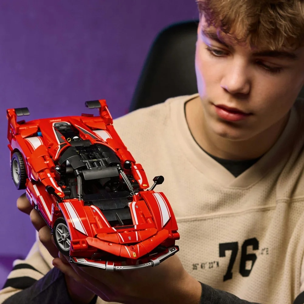 Młody mężczyzna trzyma czerwone Lego Ferrari. Uważnie się mu przygląda. Samochód ma białe paski i czarny silnik.