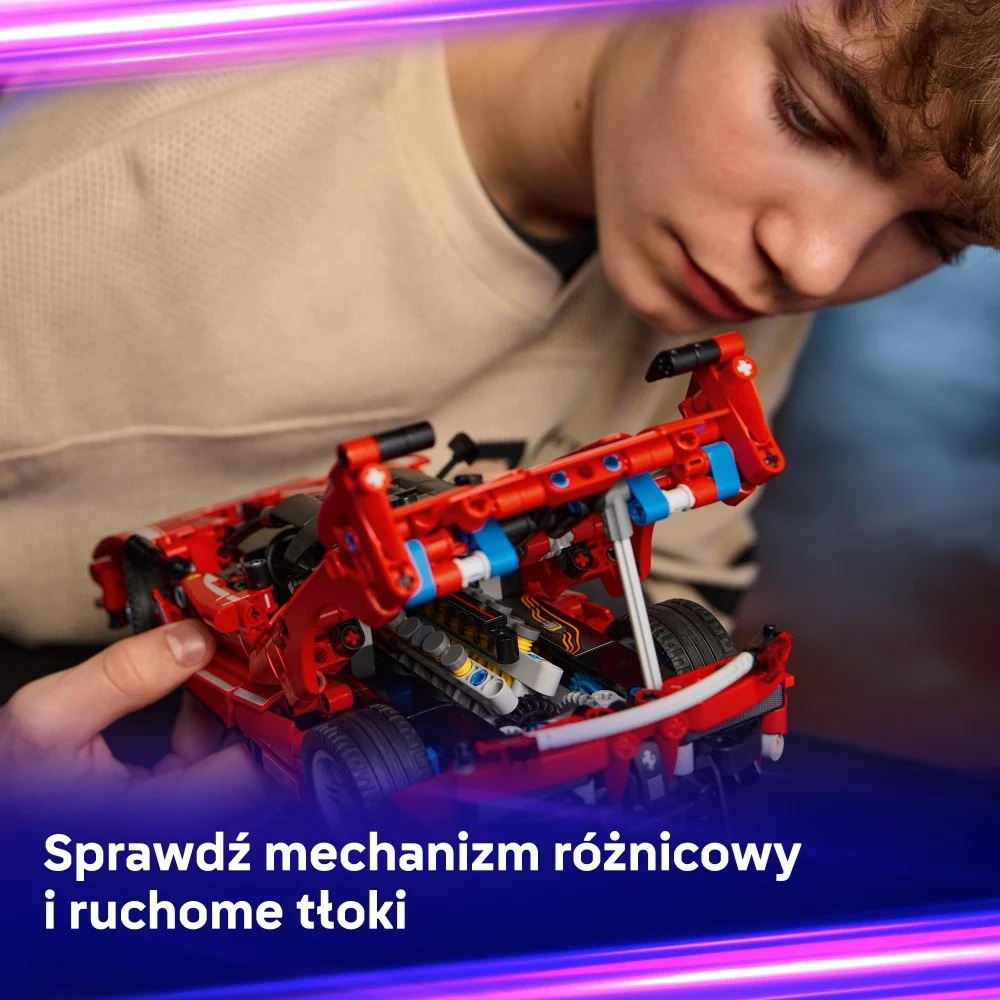 Młoda osoba bada czerwony samochodzik. Samochód ma niebieskie i czarne detale. Osoba skupia się na mechanice.