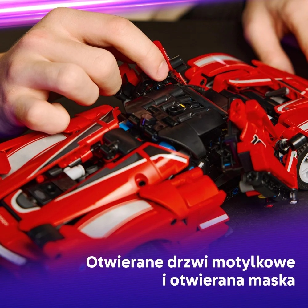 Ręka otwiera czarną część czerwonego samochodzika. Samochód ma białe paski. Tło jest rozmyte z fioletowym światłem.