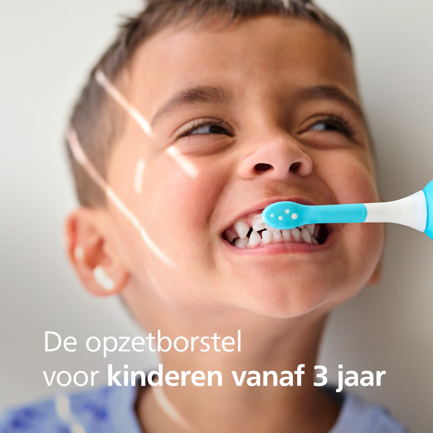 A young boy brushes his teeth with a blue and white toothbrush. He smiles, showing clean teeth. The background is plain.